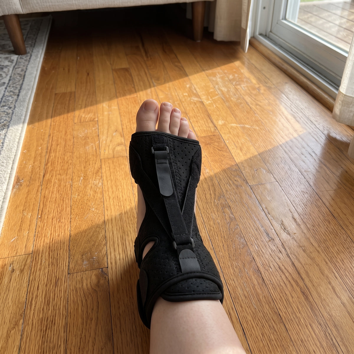 The black night splint strapped on, with the foot resting on a sunlit wooden floor