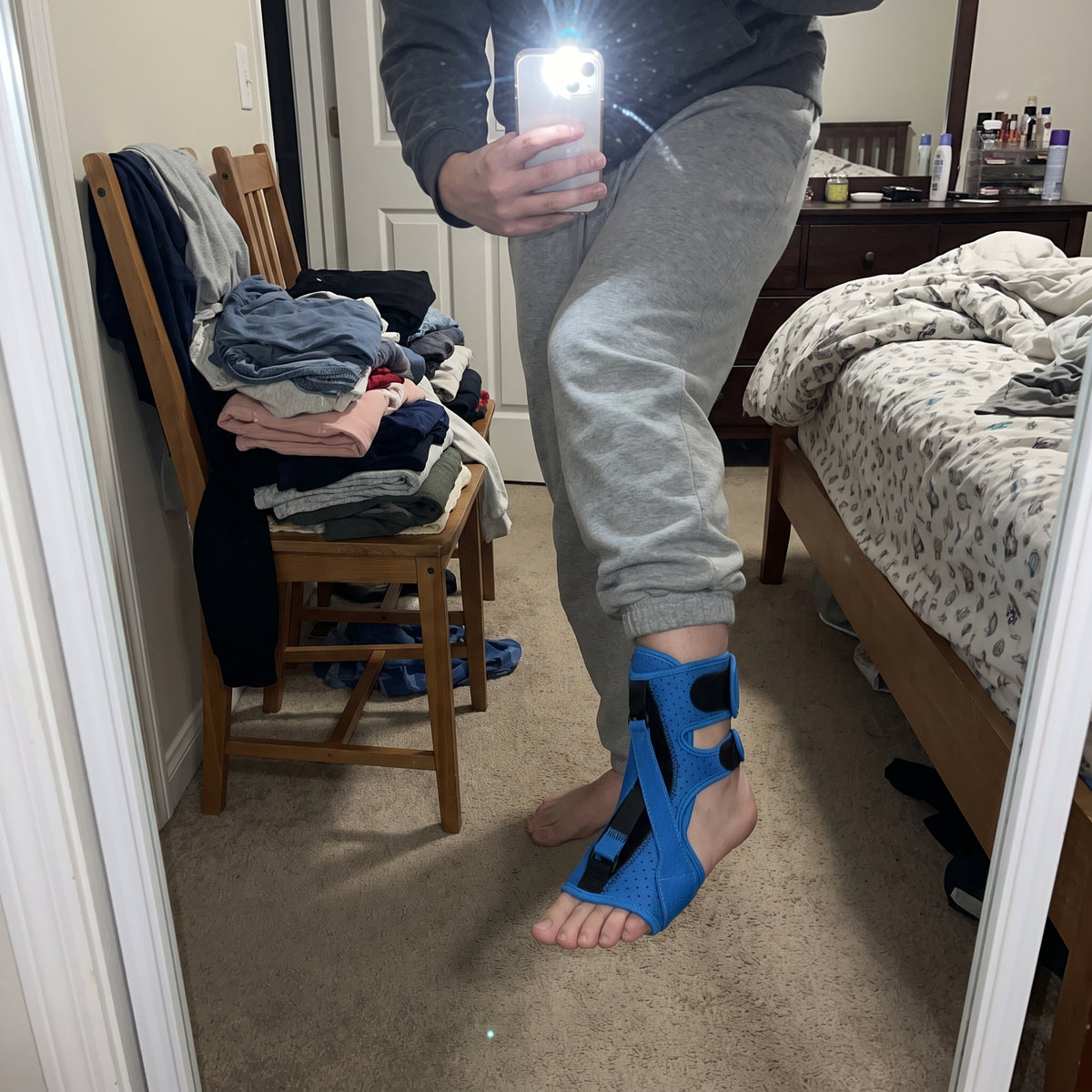 The blue night splint worn on a bare foot, photographed in a bedroom mirror