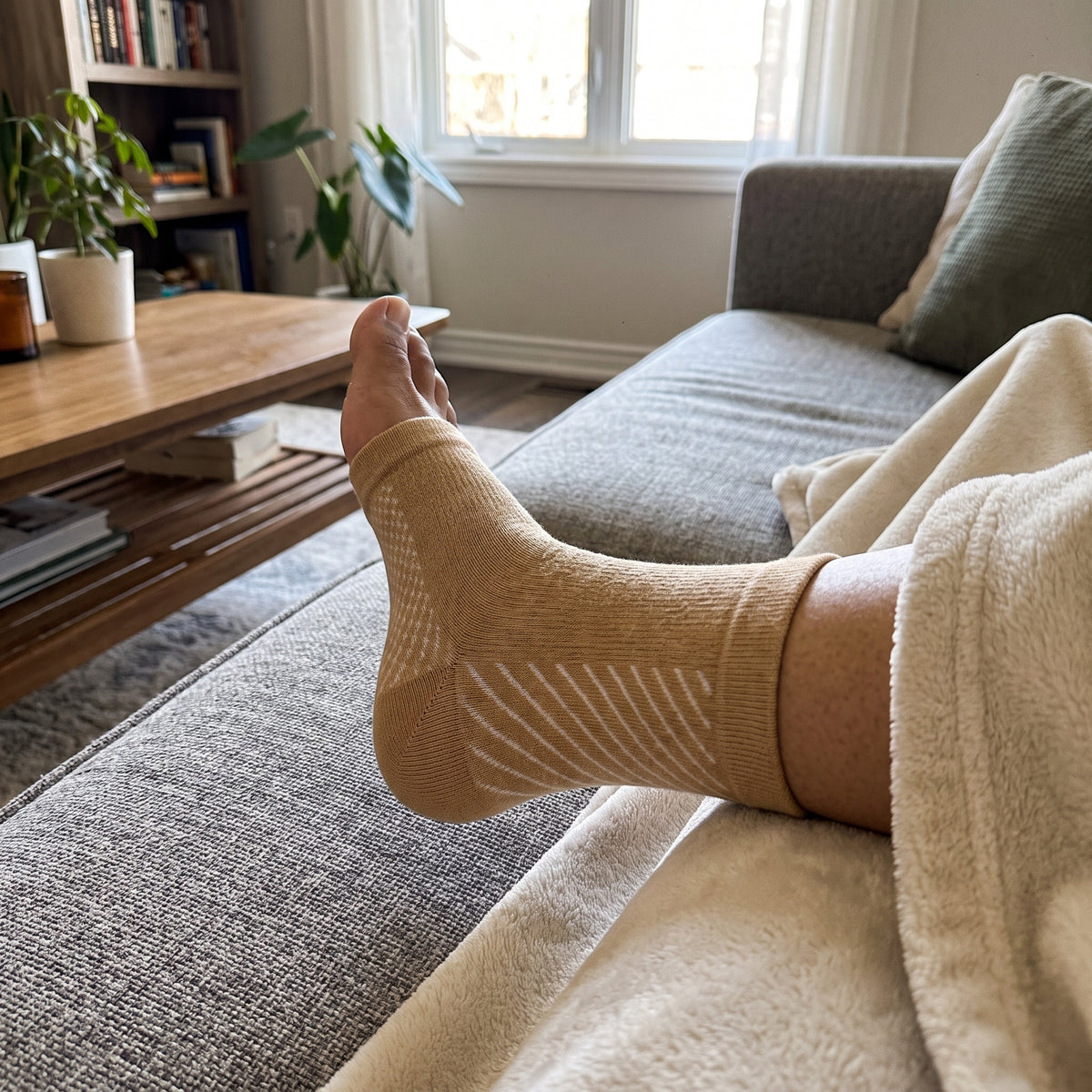 A beige compression sock worn with the foot propped up on a sofa under a blanket